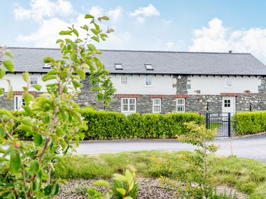 A stone and white house with multiple windows and a black gate with green shrubs and plants in front at Sgubor in Valley