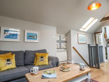 A living room with grey sofa with bee cushions and a wooden coffee table with muffins and cups at Little Brook Nottington near Weymouth