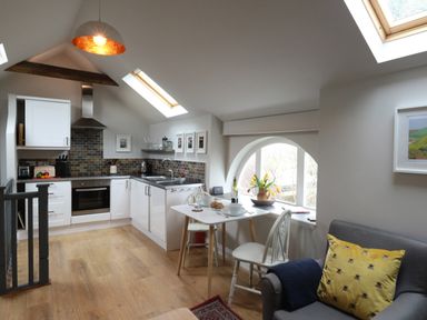 A kitchen and dining area with white cabinets a small table and chairs and a sofa with a yellow pillow at Little Brook in Nottington near Weymouth