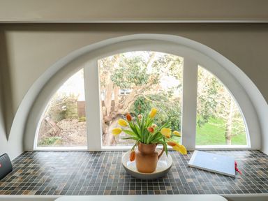 Arched window with a vase of tulips on tiled windowsill and a book at Little Brook in Nottington near Weymouth