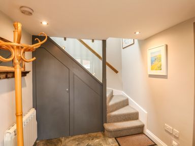 A staircase with carpeted steps and a wooden handrail next to a gray under stairs storage door and a wooden coat rack at Little Brook in Nottington near Weymouth