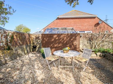 A courtyard with two wooden chairs and a round table with a flower pot at Little Brook in Nottington near Weymouth