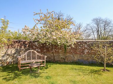 A garden with a wooden bench and table under a blooming tree by a brick wall at Little Brook in Nottington near Weymouth