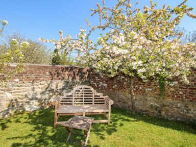 A garden with a wooden bench a small wooden table and a flowering tree by a stone wall at Little Brook in Nottington near Weymouth