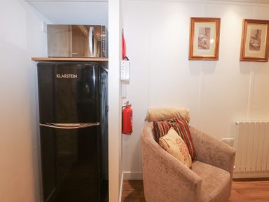 A fridge, microwave, armchair, and fire extinguisher at Orchard Lodge in Bolney
