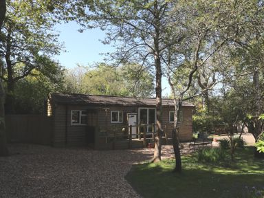 A wooden cabin with a deck surrounded by trees at Orchard Lodge Bolney