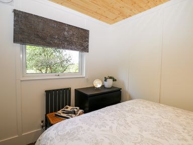 A bedroom with a bed a window a black chest of drawers and a small plant at Harvest Lodge in Wineham near Bolney