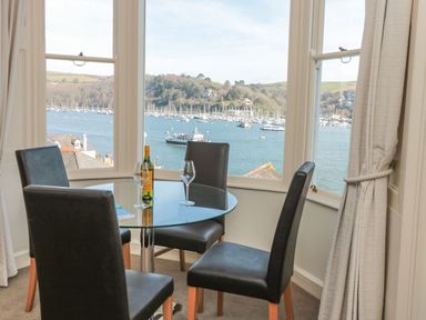 A dining area with a round glass table and four chairs overlooking a harbor with boats at 4 Dartview in Dartmouth