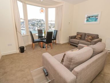 A living room with two sofas a glass dining table with four chairs and a large window overlooking a waterfront at 4 Dartview in Dartmouth