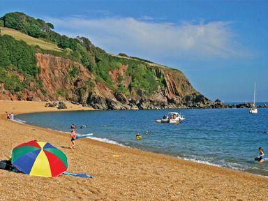 A beach with a colorful umbrella people swimming and boats near rocky cliffs at 4 Dartview in Dartmouth