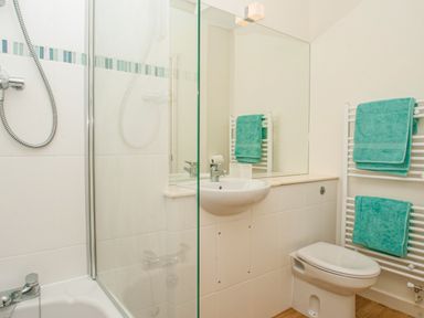 A bathroom with a bathtub and shower, a sink, a toilet, and a towel rack with teal towels at 4 Dartview in Dartmouth