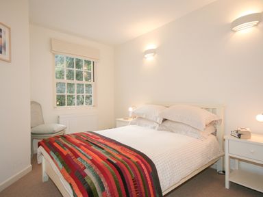 A bedroom with a bed covered with checkered bedding and a colorful quilt a chair by a window and two bedside tables with lamps at 4 Dartview in Dartmouth
