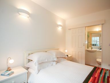 A bedroom with a bed and nightstands next to a sliding door leading to a bathroom at 4 Dartview in Dartmouth