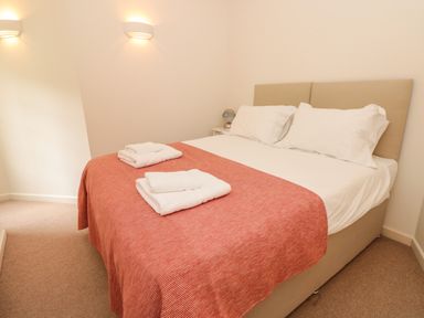 A bedroom with a bed covered in white sheets and a red blanket with folded towels on top at 4 Dartview in Dartmouth