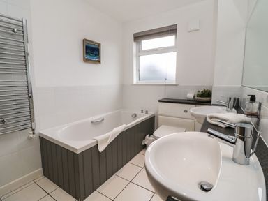A bathroom with a bathtub a toilet two sinks a window and a heated towel rail at Redwood Retallack in Retallack near St Columb Major