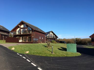 Two wooden houses with balconies on a grassy plot beside a curved paved road at Redwood Retallack in Retallack near St Columb Major