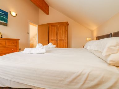 A bedroom with a bed with white linens wooden wardrobe dresser and a lamp at Redwood Retallack in Retallack near St Columb Major