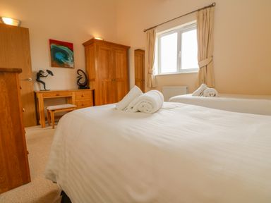 A bedroom with two single beds with towels on them a wooden desk wardrobe chair and a window with curtains at Redwood Retallack Retallack near St Columb Major