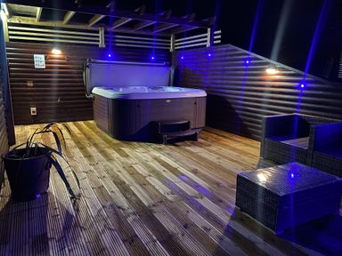 An outdoor hot tub on a wooden deck with wicker chairs and a table at Redwood Retallack in Retallack near St Columb Major