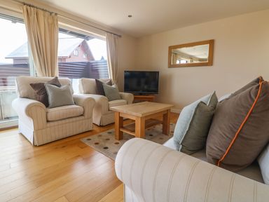 A living room with two armchairs a sofa a wooden coffee table a television and a mirror at Redwood Retallack in Retallack near St Columb Major