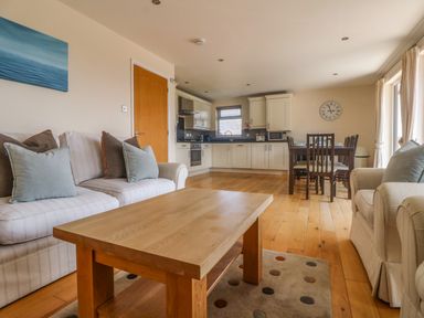 An open-plan living room with sofas a wooden coffee table kitchen cabinets and a dining table with chairs at Redwood Retallack in Retallack near St Columb Major