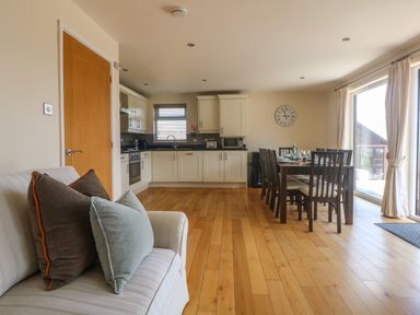 An open plan kitchen and dining area with a sofa on the left and glass doors on the right at Redwood Retallack in Retallack near St Columb Major