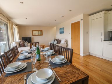A dining table set with plates bowls glasses and cutlery in a living space with sofas a TV and kitchen units at Redwood Retallack Retallack near St Columb Major