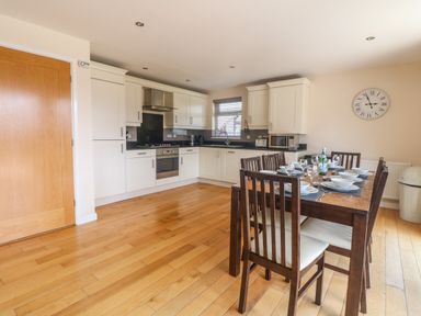 A kitchen and dining area with wooden floor a dining table set with dishes and glassware and white cabinets Redwood Retallack in Retallack near St Columb Major