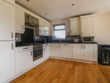 A kitchen with white cabinets wooden floor oven and microwave at Redwood Retallack in Retallack near St Columb Major