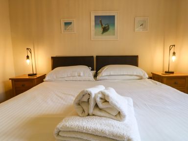 A bedroom with a large bed with white linens two bedside tables with lamps and three framed pictures on the wall at Redwood Retallack in Retallack near St Columb Major