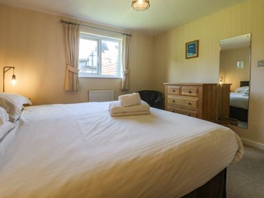 A bedroom with a bed, stacked towels on the bed, a window with curtains, a dresser, a mirror, and a chair at Redwood, Retallack in Retallack near St Columb Major