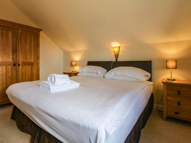 A bedroom with a double bed with white linens wooden bedside tables lamps and a wardrobe at Redwood Retallack Retallack near St Columb Major