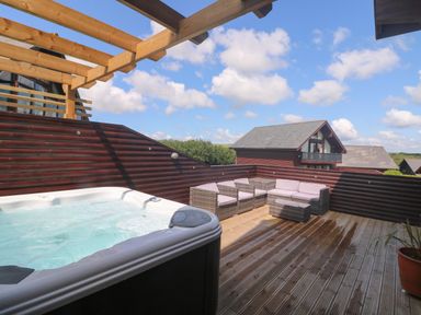 An outdoor deck with a hot tub and wicker seating set with cushions at Redwood Retallack in Retallack near St Columb Major