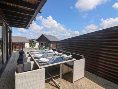 An outdoor dining area with table set for eight and chairs on a wooden deck at Redwood Retallack in Retallack near St Columb Major