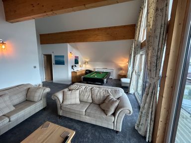 A living room with two sofas a pool table wooden beams and large windows with curtains at Redwood Retallack in Retallack near St Columb Major