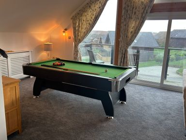 A room with a pool table next to a large window with patterned curtains at Redwood Retallack in Retallack near St Columb Major