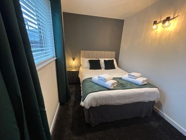 A bedroom with a double bed towels on the bed bedside table window with blinds and curtains at Redwood Retallack in Retallack near St Columb Major