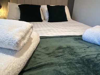 A bed with white and black pillows folded towels and a green blanket at Redwood Retallack near St Columb Major