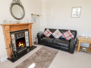 A living room with a fireplace a black leather sofa with cushions a wooden side table and a rug at The Nook in Benllech