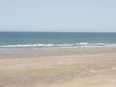 A beach with people walking and the sea in the background at The Nook in Benllech