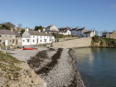 A pebble beach with boats and a stone wall next to houses at The Nook in Benllech
