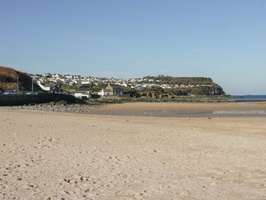 A sandy beach with rocky shoreline and houses on a hill in the background at The Nook in Benllech