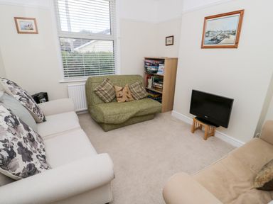 A living room with sofas a TV on a small stand a bookshelf with board games and paintings on the walls at The Nook in Benllech