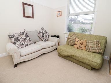 A room with a white sofa with floral pillows and a green sofa with checked and bird patterned pillows at The Nook in Benllech