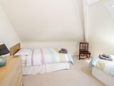 A bedroom with two single beds a wooden dresser with a lamp and a wooden chair at The Nook in Benllech