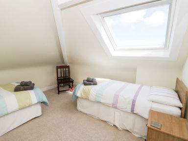 A bedroom with two single beds a wooden chair and a wooden nightstand under a skylight window at The Nook in Benllech