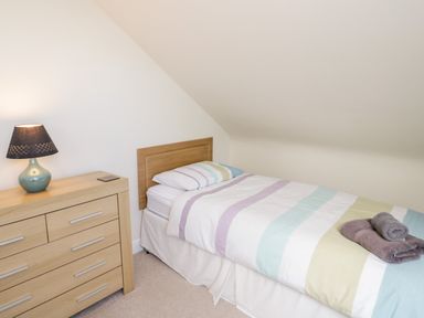 A bedroom with a single bed striped bedding wooden dresser and a table lamp at The Nook in Benllech