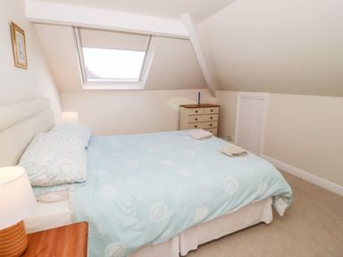 A bedroom with a double bed a window in the slanted ceiling a chest of drawers and a bedside table with a lamp at The Nook in Benllech