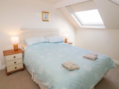 A bedroom with a bed with light blue bedding two nightstands with lamps and a skylight window at The Nook in Benllech