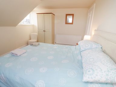 A bedroom with a bed covered in blue patterned bedding a wardrobe a chair and a wall mirror at The Nook in Benllech